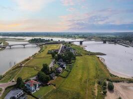 Aerial view of Nijmegen, Netherlands, featuring the Waal River, Waalbrug, green landscapes, houses, open fields, and a sunset lit sky. photo