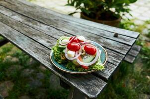 Plate of salad with lettuce, tomatoes, and onions sits on a wooden table photo