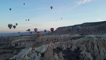 Drone flies over marble cliffs with hot air balloons in the background in Cappadocia video