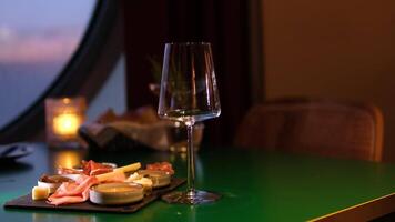 Cheese platter and red wine. Pouring red wine into glass standing on cheese board with different kinds of cheese. Nicely served selection of exquisite cheese on a black background and wine tasting video