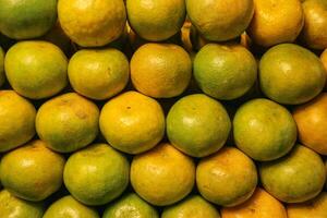 Horizontal wide angle view of fresh Thai honey tangerines with golden yellow and green peel, sweet tangy taste and textured skin, arranged as local street food. photo
