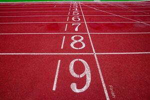 Horizontal wide shot of running track finish line, lanes 1 to 9 red surface and white stripe, symbolizing competition, motivation and victory. photo
