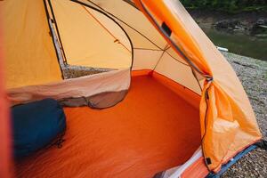 A bright orange tent is set up on the soft, inviting ground beside a gently flowing river, creating a stunning and picturesque camping scene in the beautiful and serene outdoors photo