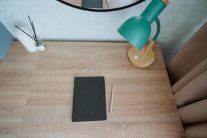 A beautifully crafted wooden desk features a bright lamp that offers soft light. A neatly arranged notebook awaits notes or thoughts to be penned with care and precision photo