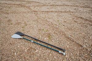 Two wooden oars are resting on the sandy ground on the beach, their smooth surfaces gleaming under the sunlight as they lay in a relaxed position, waiting to be picked up photo
