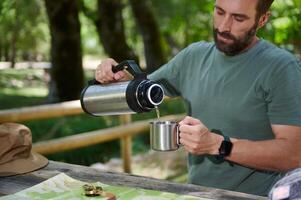 Man Pouring a Drink From a Thermos in a Wooden Outdoor Setting photo
