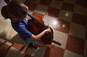 Young Musician Playing the Cello in a Well-Lit Room with Checkered Tiles photo