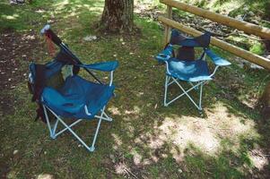 Foldable Camping Chairs in a Scenic Forest Location by a Wooden Fence and a Stream photo