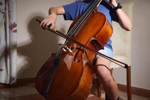 Individual playing cello with precision and emotion, showcasing the artistry of string instrument mastery in an indoor setting. Light accents enhance the polished wooden finish of the cello. photo