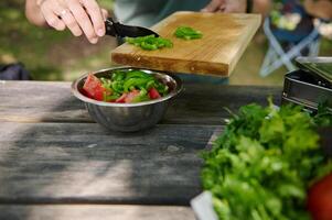 Preparing a Fresh Vegetable Salad Outdoors on a Picnic Table Surrounded by Greens photo