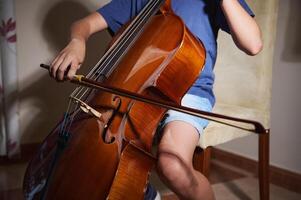 A focused young musician skillfully playing a cello indoors, emphasizing the beauty and craftsmanship of the musical instrument against a cozy and intimate setting. photo