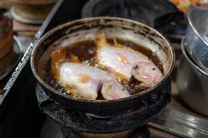 Two red tilapia fish frying with bubbling in dirty pan photo