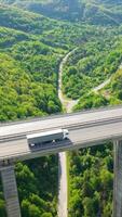 Modern Delivery Lorry Crossing Stone Bridge Roadway in Green Hilly Landscape Vertical video
