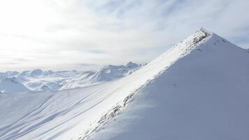 Drone shot aerial rising above a pristine snow-covered mountain peak, revealing untouched powder and ski tracks from freeride and alpine skiing in winter wilderness video