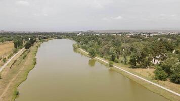 Aerial fly over view of Rustavi Central Park featuring a calm lake surrounded by trees and walking paths, popular for recreation cycling and nature enjoyment in Georgia video