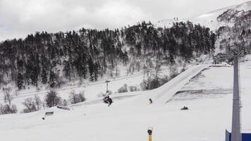 Snow-covered ski slope with active chairlift, snowmobile on piste, and forest backdrop. Winter sport scene, mountain resort infrastructure, snowy recreation. video