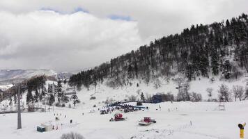 Europe - 2024- Machines prepare ski slope for upcoming event at winter resort. Snow-covered landscape, forested hills, ski lift infrastructure and competition zone in view. video