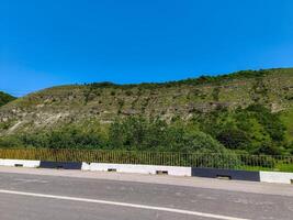 A road with a yellow and black striped barrier on the side. The road is empty and the sky is clear photo