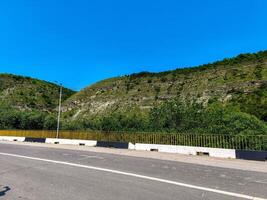 A road with a yellow and black fence on the side. The road is empty and the sky is blue photo