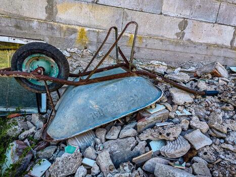 A wheelbarrow is laying on its side in a pile of rubble. The wheel is missing, and the handle is bent. The scene is chaotic and disorganized, with debris scattered everywhere photo