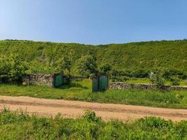 A green hillside with a stone wall and a gate. The gate is open and the road is dirt photo