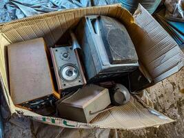 A box full of old electronics including a TV, speakers, and a radio. The box is open and the electronics are scattered around it photo