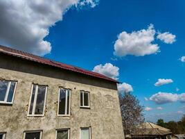 A building with a red roof and a blue sky in the background. The sky is filled with clouds, and the building has a lot of windows photo