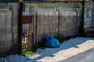 A blue plastic bag is sitting on the ground next to a gate. The gate is rusted and the bag is placed on the ground in front of it photo