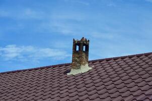 A chimney on a roof with a blue sky in the background. The chimney is covered in rust and has a small hole in it photo