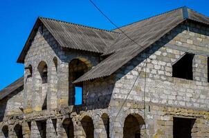 A large, old building with a gray roof and white walls. The building appears to be abandoned and in disrepair photo