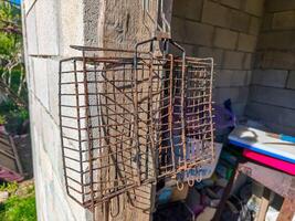 A rusty metal cage is hanging from a wall. The cage is old and has a lot of rust on it. The cage is hanging from a wooden beam photo
