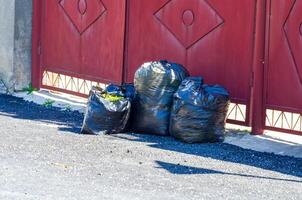 A pile of trash bags are sitting on the ground next to a red gate. The bags are black and appear to be full. The scene gives off a sense of neglect and disorganization photo