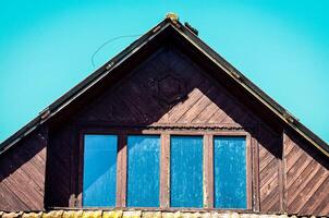 A house with a slanted roof and a window with three panes. The window is dirty and the roof is brown photo