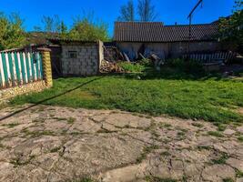 A small house with a yard and a fence. The yard is full of grass and weeds. The house is old and has a lot of rust photo