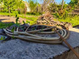 A bunch of garden hose is laying on a cement slab. The hose is tangled and he is old. The scene is somewhat messy and disorganized photo