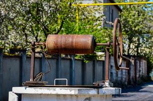 A rusty old metal object with a chain wrapped around it. The chain is attached to a metal rod. The object is sitting on a cement block. The scene is quiet and peaceful photo