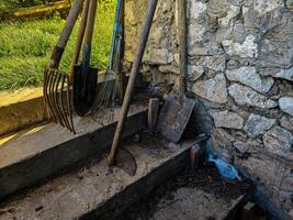 A pile of tools including a shovel, a rake, and a pitchfork are on a set of steps photo