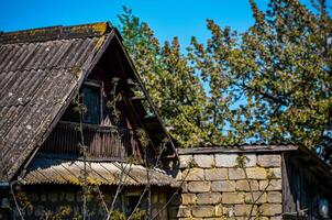 A house with a slanted roof and a balcony. The balcony is covered in ivy. The house is surrounded by trees and has a stone wall photo