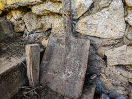 A rusty shovel is leaning against a wall. The shovel is old and worn, and it is a bit of a mess. The wall behind the shovel is made of stone, and it seems to be a part of a larger structure photo