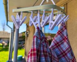 A white clothesline with a few clothes hanging on it. The clothes are mostly plaid and red photo