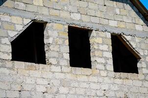 A building with three windows and a roof. The windows are open and the building is empty. Scene is somewhat lonely and abandoned photo