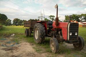 A red tractor with a trailer parked in a field photo