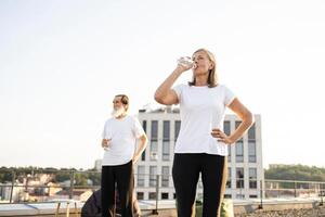 Elderly man and woman in open rooftop setting, enjoying refreshing water after workout outdoors in city. Representing healthy lifestyle, fitness activities, active retirement and responsible hydration photo