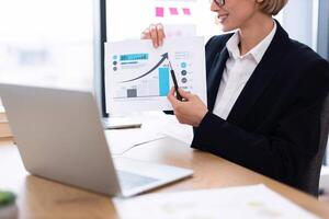 Business professional displaying economic data during meeting using printed chart, laptop on desk photo