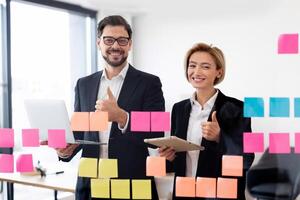 Two adult business professionals, man and woman, discussing strategy while using colorful sticky notes photo
