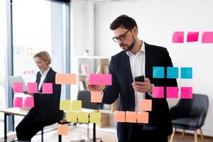 Corporate employees collaborating using glass board with colorful notes in professional workspace setting. photo