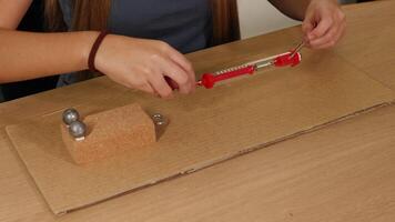 Hands manipulate a spring scale to measure force on a weighted block on cardboard, demonstrating friction principles video