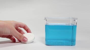 A hand drops a soap bar into a clear container of blue water, observing its sinking behavior video