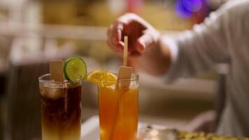 A bartender stirs two cocktails with citrus garnishes in a warmly lit bar setting video