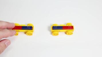 Hands manipulate toy cars with magnets, illustrating attraction and repulsion on a white surface under bright lighting video